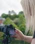 Blonde Frau bedient eine Kamera auf einem Stativ vor grünem Hintergrund.
