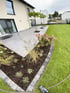 Moderne Terrasse mit grauen Fliesen, angrenzendem Blumenbeet mit Rindenmulch und einer gepflegten Rasenfläche.