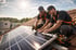 Zwei Solarteure installieren Solarmodule auf einem Ziegeldach unter blauem Himmel mit Sonnenschein.
