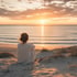Eine Frau sitzt in den Dünen am Strand und blickt auf den Sonnenaufgang über dem Meer.