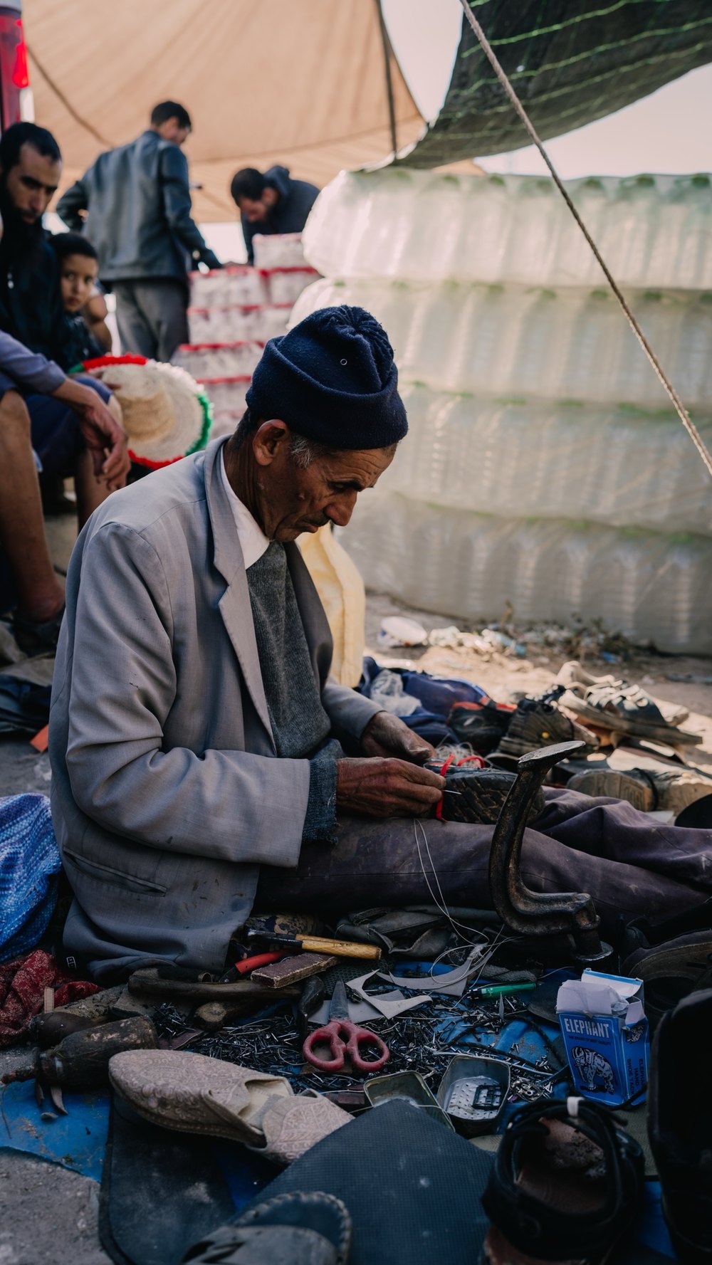 Älterer Mann sitzt zwischen seinen Waren auf dem Wochenmarkt