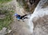 Person seilt sich an einem Wasserfall ab, trägt blauen Helm und Neoprenanzug.