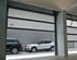 Offene Garage mit zwei geparkten Autos, ein schwarzer und ein weißer SUV, vor einer grauen Wand aus Ziegelsteinen.