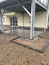 Geflieste Terrasse unter einem Balkon aus Stahl mit einer Einfassung aus dunklen Pflastersteinen vor einem Wohnhaus.