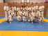 Gruppe von fünfzehn Karatekas in weißen Gis und braunen/schwarzen Gürteln posiert auf blauer und gelber Matte.
