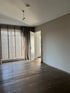 Leerer Raum mit dunklem Holzboden, hellgrauen Wänden, großer Fensterfront mit Jalousien und Vorhängen.