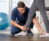 Male therapist in blue scrubs examines patient’s ankle for rehab care