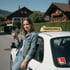 Fahrschuelerin mit Schluessel neben dem Schulfahrzeug im Sonnenschein