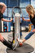 A man and woman perform leg stretches on a Power Plate vibration platform in a physical therapy clinic.