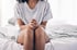 Woman sitting on bed with hands clasped in discomfort