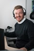 Fabian Roßmann mit Headset am Schreibtisch bei der Beratung von Bauunternehmen.