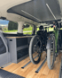 Zwei Mountainbikes im Heck eines Campers, der Van hat einen Holzboden und eine Küchenzeile.