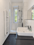 Modernes Badezimmer mit weißem Waschbecken, Handtuchheizkörper und begehbarer Glasdusche vor einem Fenster ins Grüne.