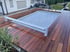 Ein rechteckiger Außenpool mit geschlossener Lamellenabdeckung in einer Terrasse aus dunklem Echtholz.