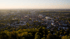 Panoramablick auf eine Stadt mit vielen Bäumen bei Sonnenuntergang, mit einem Horizont in der Ferne.