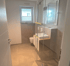 Modernes Badezimmer mit weißer Toilette, Waschbecken auf Holzplatte und Glasduschkabine.