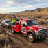 Towing Sandy winch out and recovery service pulling a stuck sedan from deep mud with a tow truck in a remote off-road area.