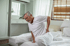 A senior man on a bed holds his back in pain.
