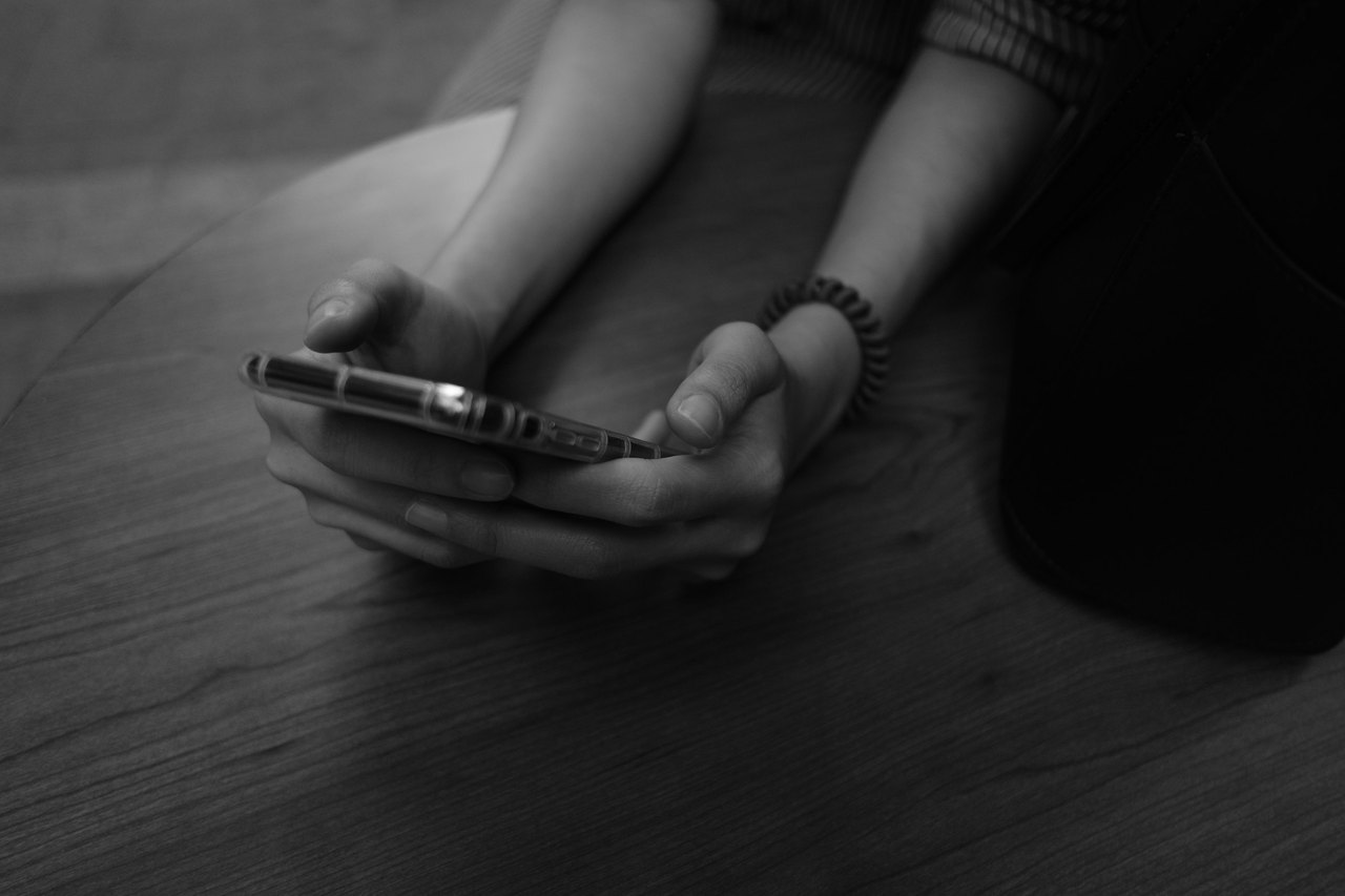 Zwei Hände halten ein Smartphone über einer Tischplatte aus Holz, in Schwarzweiß.
