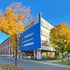 Modernes blau-weißes Gebäude mit gelben Bäumen im Herbst, sonniger Himmel, Straße und Bürgersteig.