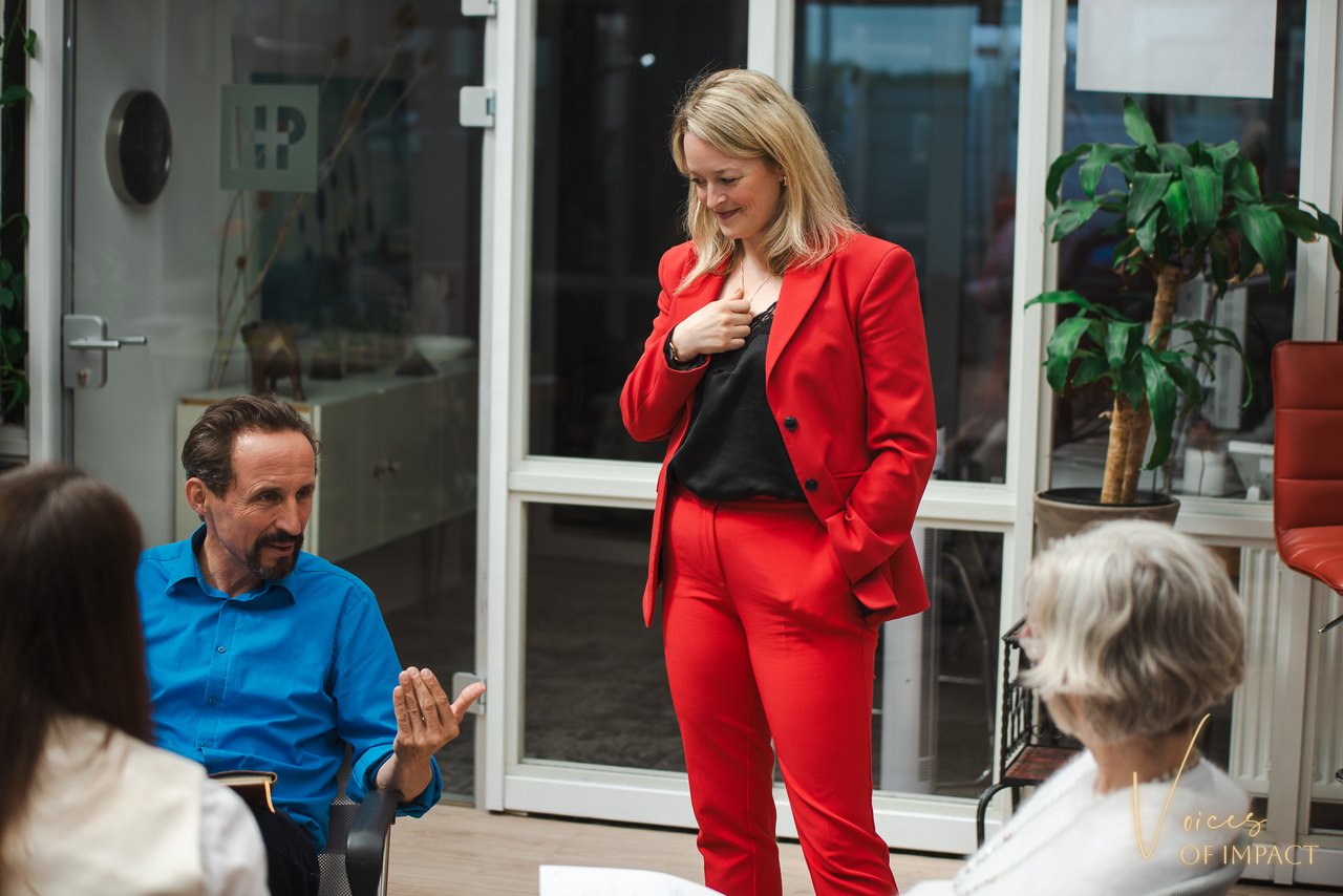 Mandy-Marie Mahrenholz spricht im roten Anzug vor einer sitzenden Gruppe