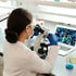 A scientist examines samples under a microscope.
