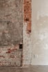 Abgeblätterte Ziegelmauer, Putz und weiße Wand mit Steckdose und Kabel.