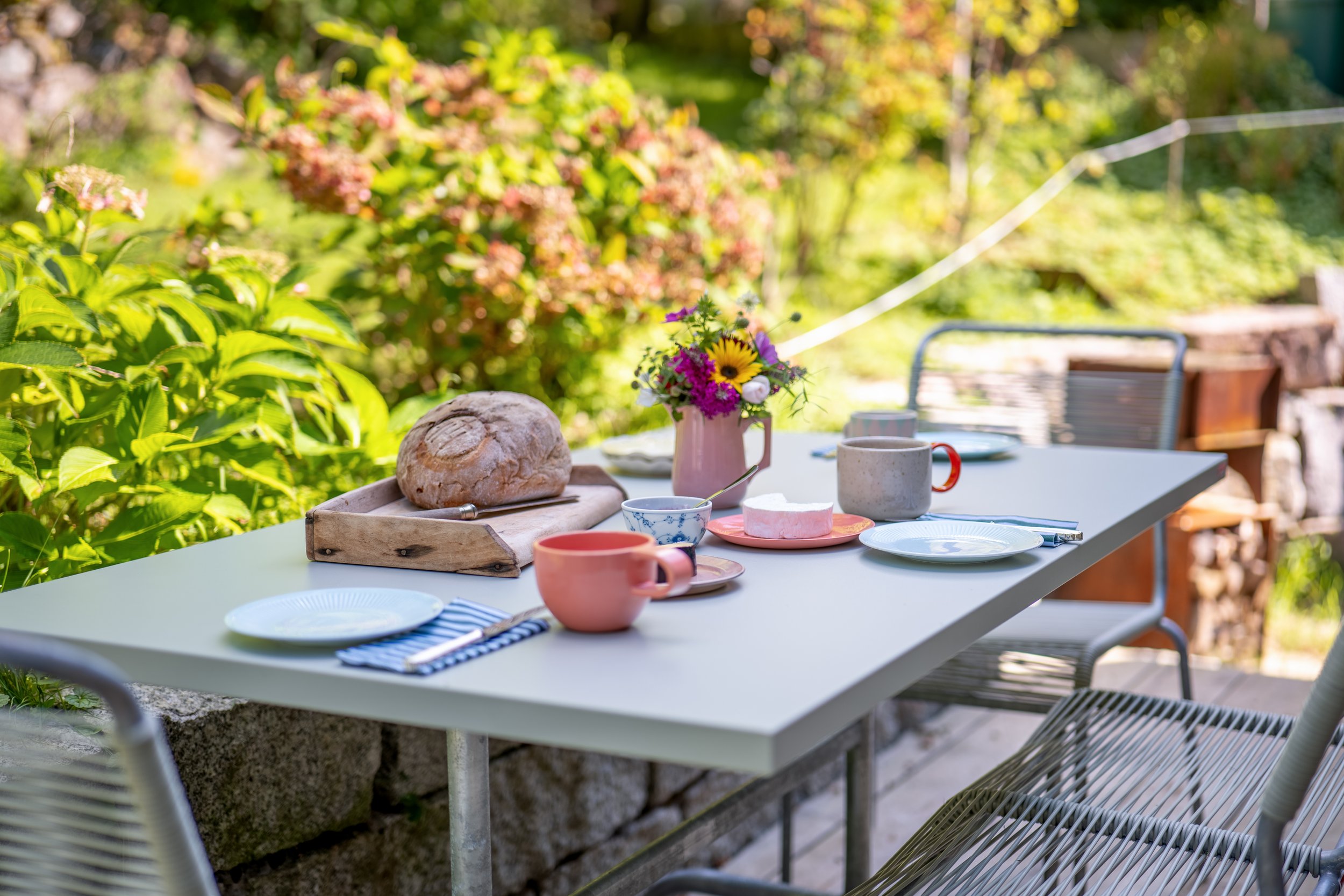 Gedeckter Frühstückstisch auf der Terrasse mit Brot, Blumen und Tassen