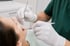 Zahnarzt in grüner Kleidung untersucht die Zähne einer Patientin mit Mundspiegel und Sonde.