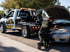 An Eastvale Towing professional inspects the engine of a silver car with an open hood next to a white tow truck.