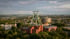 Das Deutsche Bergbau-Museum Bochum mit seinem grünen Fördergerüst überragt die bewaldete Stadtlandschaft bei bewölktem Himmel.