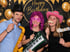 Drei Personen mit lustigen Requisiten vor einem "Happy Birthday"-Hintergrund.