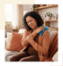 A woman sitting on a sofa wincing in pain while holding a blue gel ice pack to her shoulder.