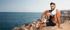 young fit male sitting on a rock at the edge of the sea, wearing black trunks