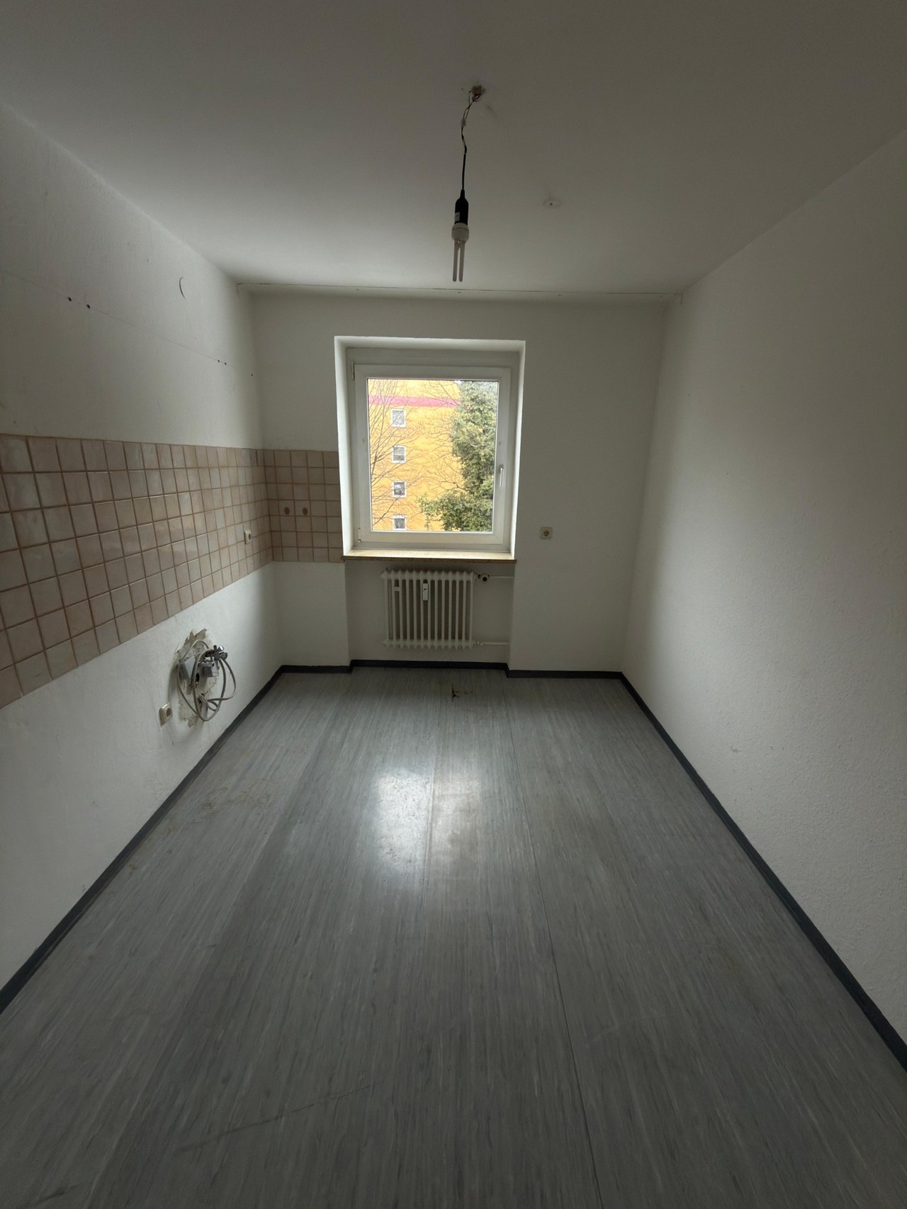 Leere Küche mit freigelegten Anschlüssen und Fliesenwand nach dem Rückbau