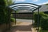 Ein Carport mit gewölbtem, durchsichtigem Dach über einem gepflasterten Weg.