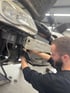 Ein Mann mit Bart repariert die Front eines Autos in einer Werkstatt.