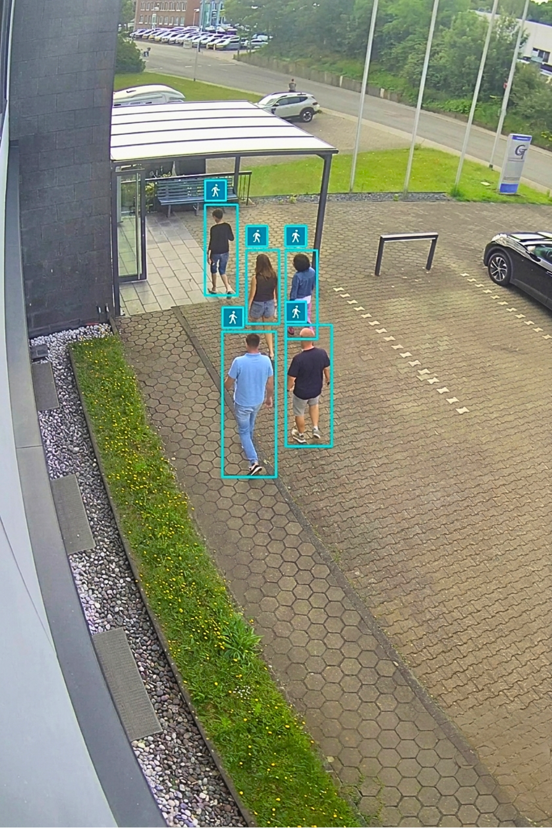 Überwachungskamera-Ansicht von Passanten auf einem gepflasterten Gehweg mit digitaler Personenerkennung durch blaue Rahmen.