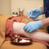 A clinician in blue gloves administers a needle injection into a patient's knee during a medical procedure.