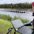 Ein Ruder-Achter trainiert auf einem Fluss, während eine Person am Ufer Daten auf einem Laptop am Fahrradlenker analysiert.