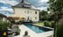 Ein moderner Garten mit rechteckigem Pool, Sonnenschirm, Liegestühlen und einem zweistöckigen Haus im Hintergrund.