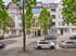 Mehrstöckige Wohnhäuser im Altbau-Stil an einer gepflasterten Straße mit parkenden Autos und grünen Bäumen.