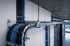 Bündel blauer und schwarzer Kabel verlaufen entlang eines Metallkabelkanals an einer grauen Wand und Decke.