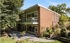 Mid-century modern brick house with large windows, balconies, and a landscaped patio surrounded by trees.