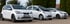 Drei weiße Elektro-Kleinwagen, darunter ein Seat Mii electric, parken nebeneinander im Freien vor grünen Hecken.