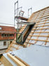 Ein eingebautes Dachfenster auf einem mit Holzlatten und Bauder-Folie vorbereiteten Steildach neben einem Gerüst.