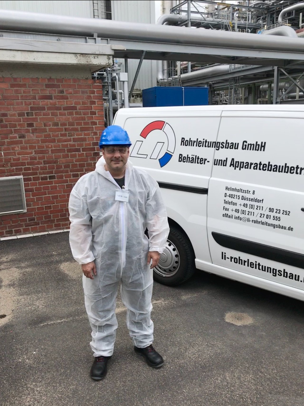 Mitarbeiter in Schutzanzug und Helm vor Firmenwagen der LI Rohrleitungsbau GmbH auf einem Industriegelände