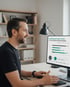Lächelnder Mann am Schreibtisch, der auf einen Computermonitor mit einer Kostenübersicht schaut.