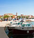 Boote liegen am Kai eines Hafens mit Palmen und Gebäuden im Hintergrund in Pakostane.