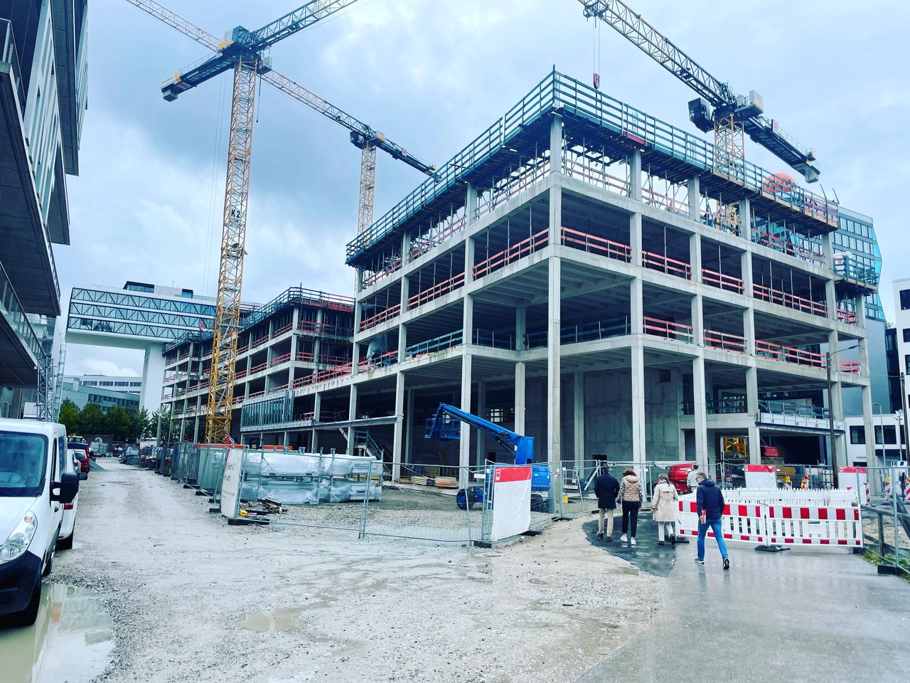 Baustelle mit zwei großen Kränen und einem mehrstöckigen Rohbau unter bewölktem Himmel.